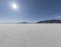 an empty desert plain with mountains in the background and a bright sky and sun in the middle