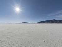 an empty desert plain with mountains in the background and a bright sky and sun in the middle