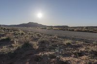 a desert road with a sign on it near a desert and mountain scene during the sun rising