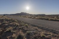 a desert road with a sign on it near a desert and mountain scene during the sun rising