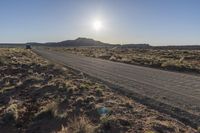 a desert road with a sign on it near a desert and mountain scene during the sun rising