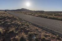 a desert road with a sign on it near a desert and mountain scene during the sun rising