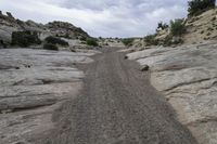 the gravel road goes over a rocky cliff face to some rocks below it and into the canyon