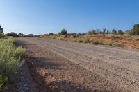 a truck is parked next to the side of a dirt road with weeds and rocks in front