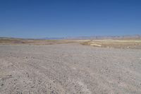 the dirt road winds through a dry desert plain against a blue sky and mountain range in the distance