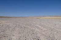 the dirt road winds through a dry desert plain against a blue sky and mountain range in the distance