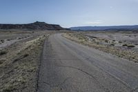 a large dirt field near a small paved highway with the sun behind it with mountains on either side