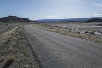 a large dirt field near a small paved highway with the sun behind it with mountains on either side