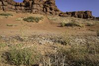 a dirt road that has many rocks and bushes in the area behind it and another red rock