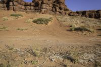 a dirt road that has many rocks and bushes in the area behind it and another red rock