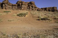 a dirt road that has many rocks and bushes in the area behind it and another red rock