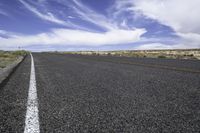 the road on a sunny day stretches out towards the horizon and into a vast desert landscape