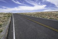 the road on a sunny day stretches out towards the horizon and into a vast desert landscape