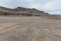 an empty field next to a big mountain with rocks in the background of the picture