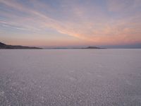 there are some rocks standing out in the snow and sunset sky behind them, on a plain near a small island