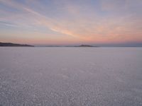 there are some rocks standing out in the snow and sunset sky behind them, on a plain near a small island