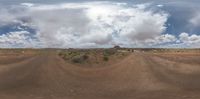 a dirt road in an empty barren area with a cloudy sky above it and mountains in the background