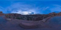 a fish eye view of rock formations in the desert at dusk with cloudy skies above