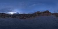 a fish eye view of rock formations in the desert at dusk with cloudy skies above