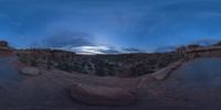 a fish eye view of rock formations in the desert at dusk with cloudy skies above