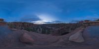 a fish eye view of rock formations in the desert at dusk with cloudy skies above