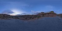 a fish eye view of rock formations in the desert at dusk with cloudy skies above