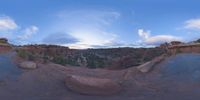 a fish eye view of rock formations in the desert at dusk with cloudy skies above