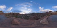 a fish eye view of rock formations in the desert at dusk with cloudy skies above