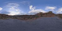 a fish eye view of rock formations in the desert at dusk with cloudy skies above