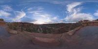 a fish eye view of rock formations in the desert at dusk with cloudy skies above