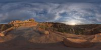 a fish eye view of rock formations in the desert at dusk with cloudy skies above