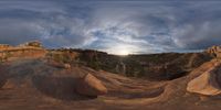 a fish eye view of rock formations in the desert at dusk with cloudy skies above