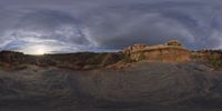 a fish eye view of rock formations in the desert at dusk with cloudy skies above