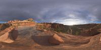 a fish eye view of rock formations in the desert at dusk with cloudy skies above