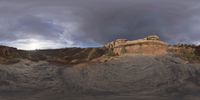 a fish eye view of rock formations in the desert at dusk with cloudy skies above