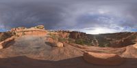 a fish eye view of rock formations in the desert at dusk with cloudy skies above