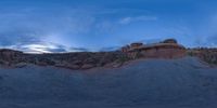 a fish eye view of rock formations in the desert at dusk with cloudy skies above