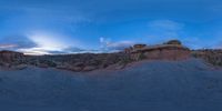 a fish eye view of rock formations in the desert at dusk with cloudy skies above