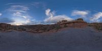 a fish eye view of rock formations in the desert at dusk with cloudy skies above