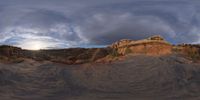 a fish eye view of rock formations in the desert at dusk with cloudy skies above