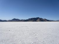 an expanse of white sand in the middle of mountains and a body of water in the background