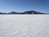 an expanse of white sand in the middle of mountains and a body of water in the background