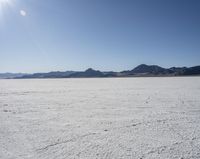 an expanse of white sand in the middle of mountains and a body of water in the background