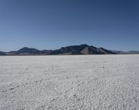 an expanse of white sand in the middle of mountains and a body of water in the background