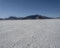 an expanse of white sand in the middle of mountains and a body of water in the background