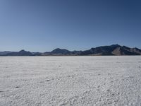 an expanse of white sand in the middle of mountains and a body of water in the background