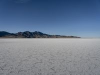 an expanse of white sand in the middle of mountains and a body of water in the background