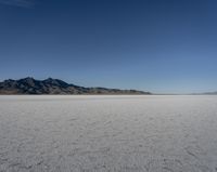 an expanse of white sand in the middle of mountains and a body of water in the background