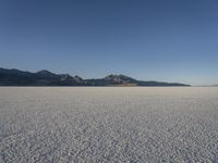 an expanse of white sand in the middle of mountains and a body of water in the background