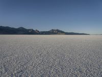 an expanse of white sand in the middle of mountains and a body of water in the background